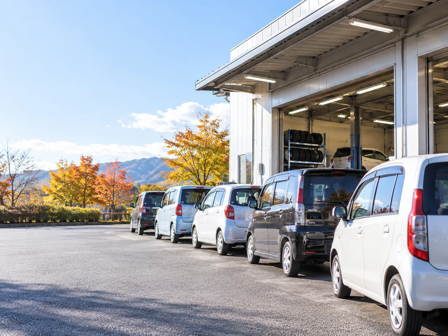 工場前に並ぶ車両と秋の山並み